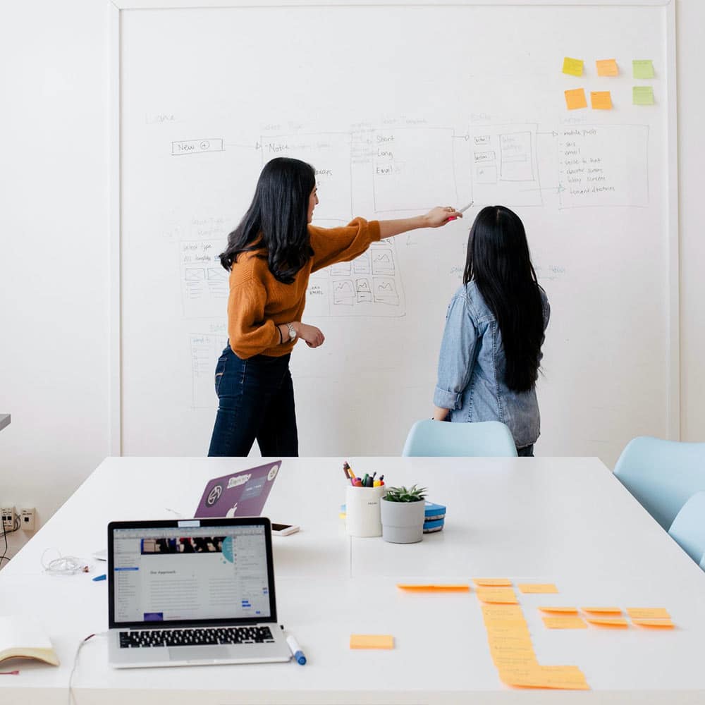 a lady explaining to another lady images on a whiteboard